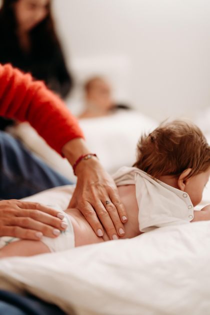 Infante disteso prono massaggiato sulla schiena da due mani di adulto
